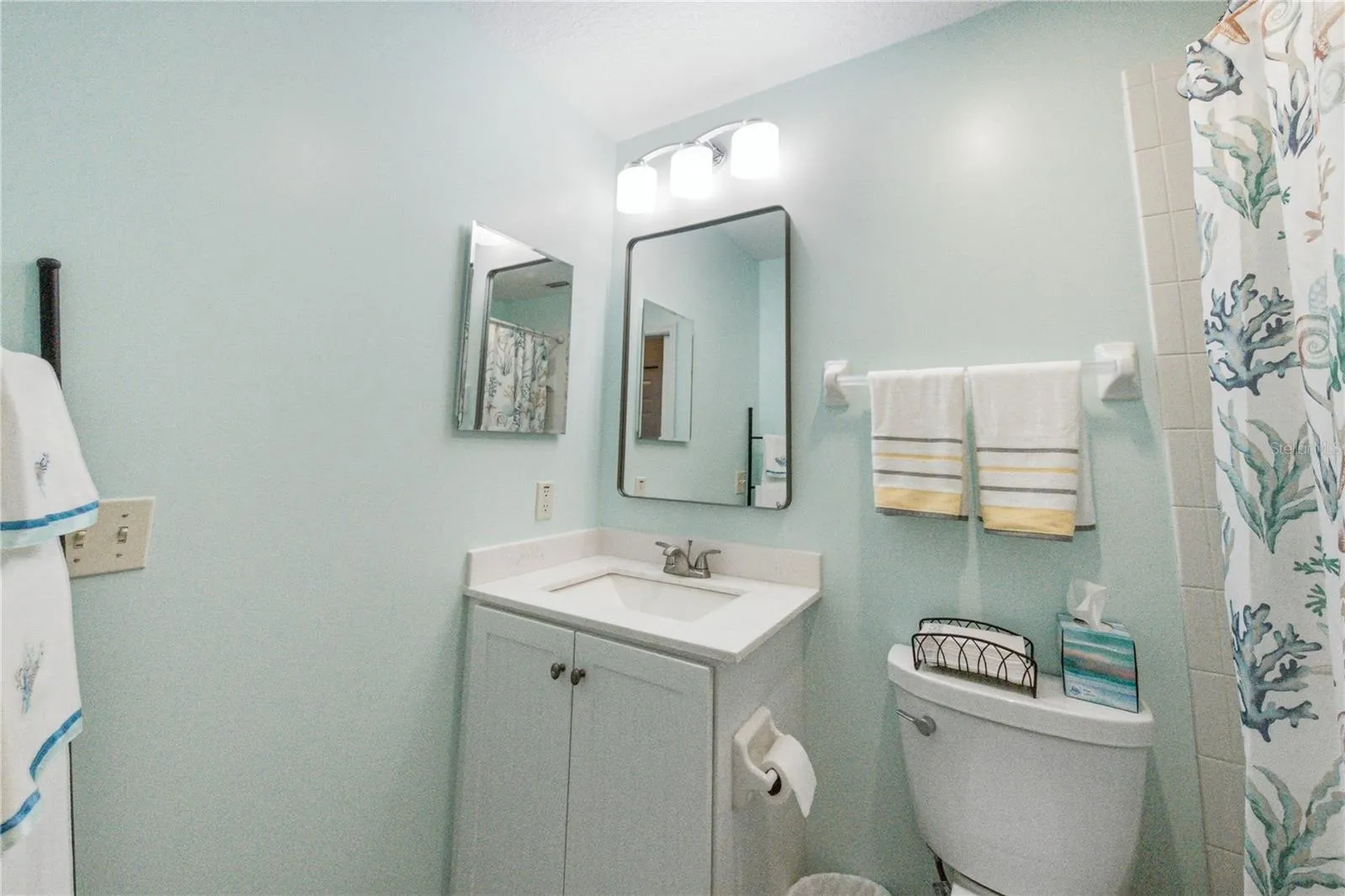 The recently remodeled guest bathroom has an elevated vanity with stone countertop, upgraded plumbing and lighting fixtures, and elongated stool.