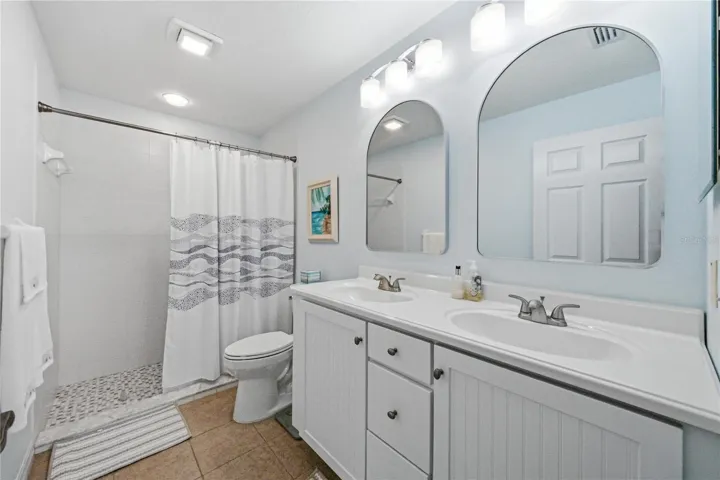 The recently remodeled primary bathroom has a large stall shower with ceramic tile surround, elevated vanity with 2 sinks in a stone counter, elongated stool, upgraded lighting, plumbing and mirrors.
