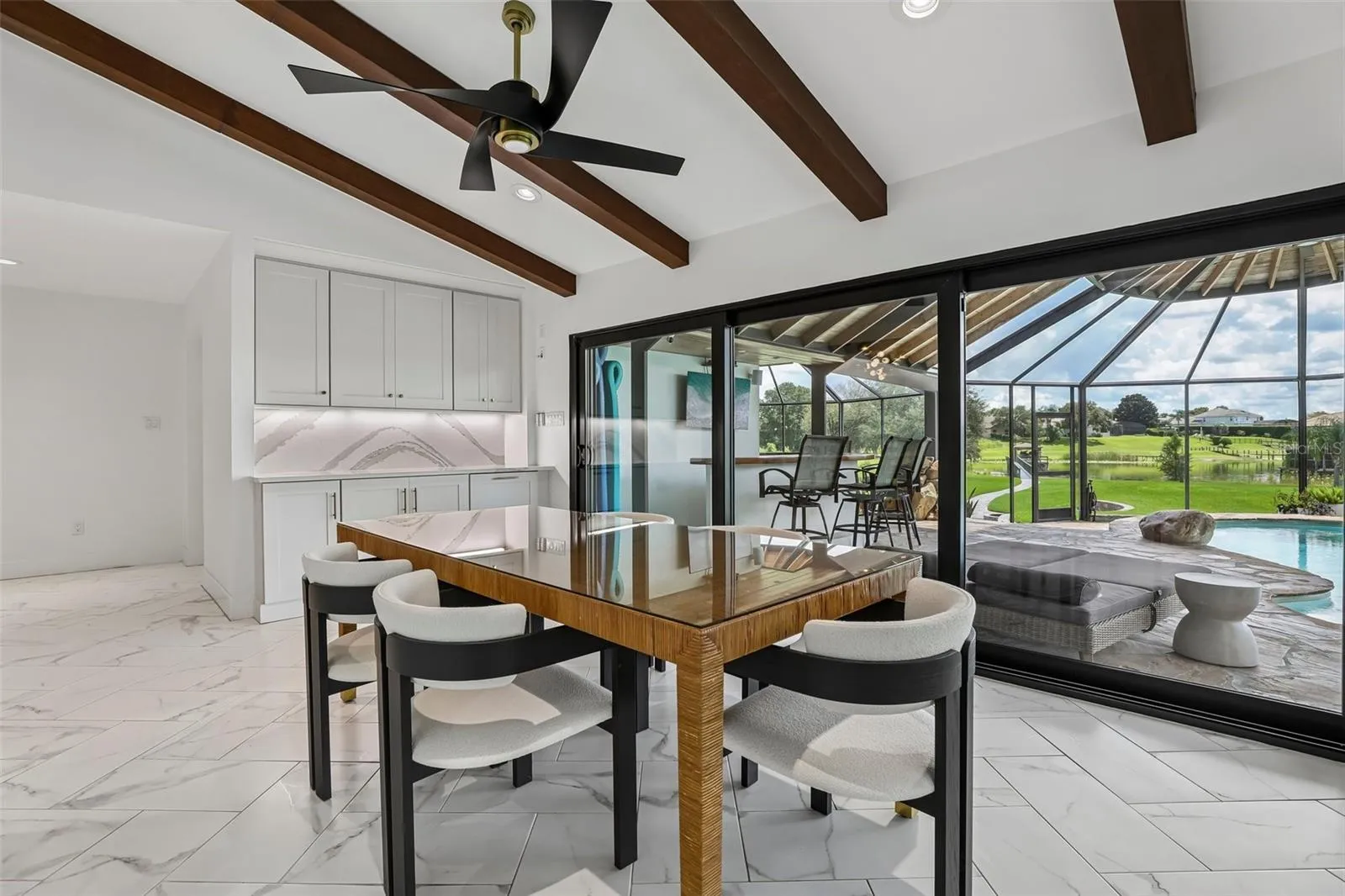 View of sun room with beverage bar, wall of sliders that retract, open to the pool overlooking the lake.