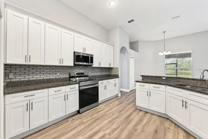 The well-appointed kitchen features GRANITE COUNTERTOPS, timeless cabinetry topped with crown molding, STAINLESS STEEL APPLIANCES, a chic tiled backsplash, breakfast bar and pantry storage.