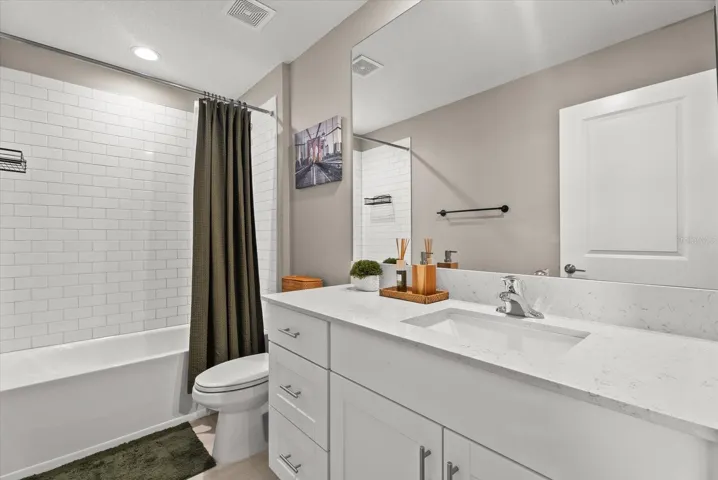 Full guest bathroom with a spacious vanity and tiled tub-and-shower combination.