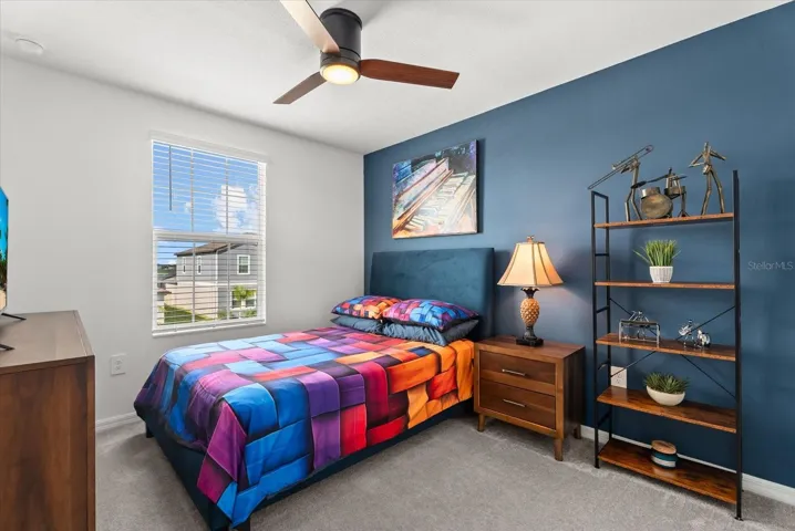 Additional bedroom featuring a ceiling fan, accent wall, and natural light.