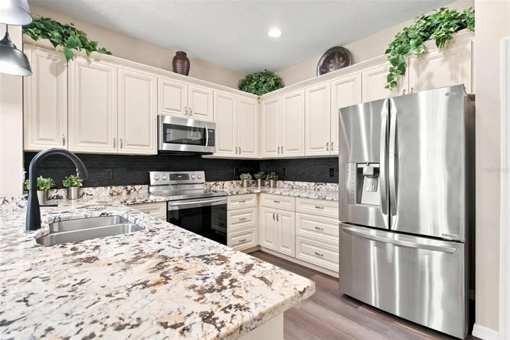 Kitchen overlooks dining and living area. Kitchen features recessed lighting, upgraded cabinets with soft close features, stainless steel appliances, backsplash, and upgraded granite countertops.