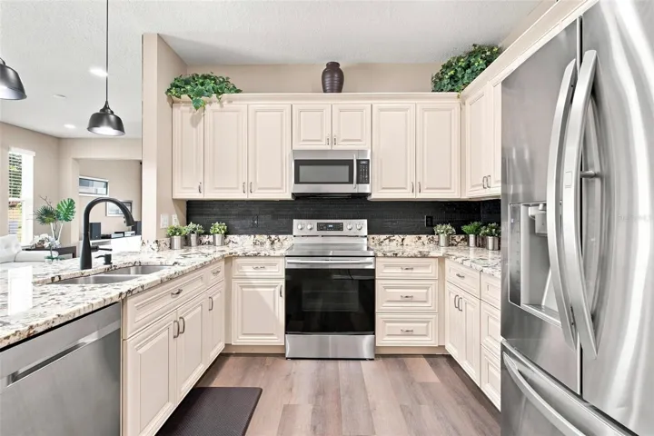 Kitchen overlooks dining and living area. Kitchen features recessed lighting, upgraded cabinets with soft close features, stainless steel appliances, backsplash, and upgraded granite countertops.