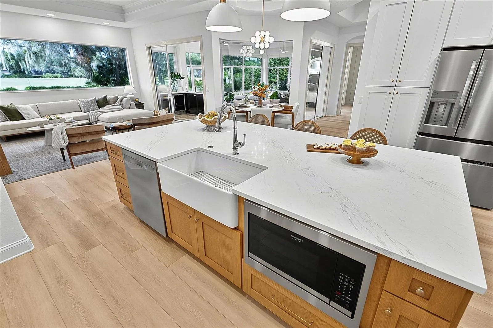 Kitchen Island with farm sink, dishwasher and microwave showing refrigerator with wall of pantry cabinets and family room