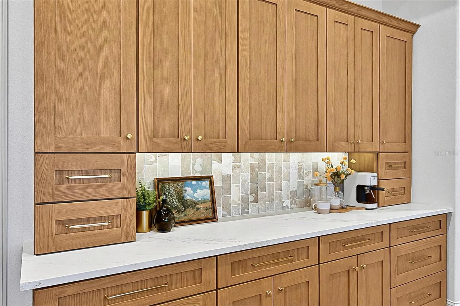 Full wall of Custom Wood soft close cabinets with under-mount lighting against the stunning tile and quartz countertops