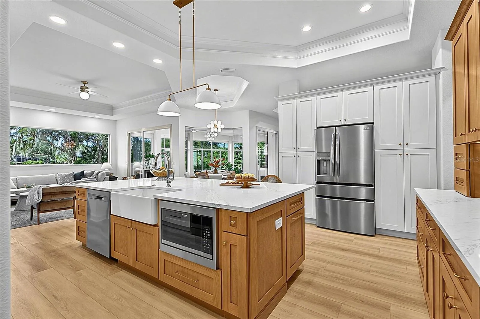 Kitchen Island with farm sink, dishwasher and microwave showing refrigerator with wall of pantry cabinets and family room