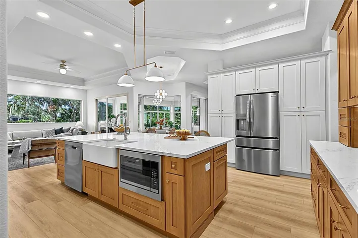 Kitchen Island with farm sink, dishwasher and microwave showing refrigerator with wall of pantry cabinets and family room