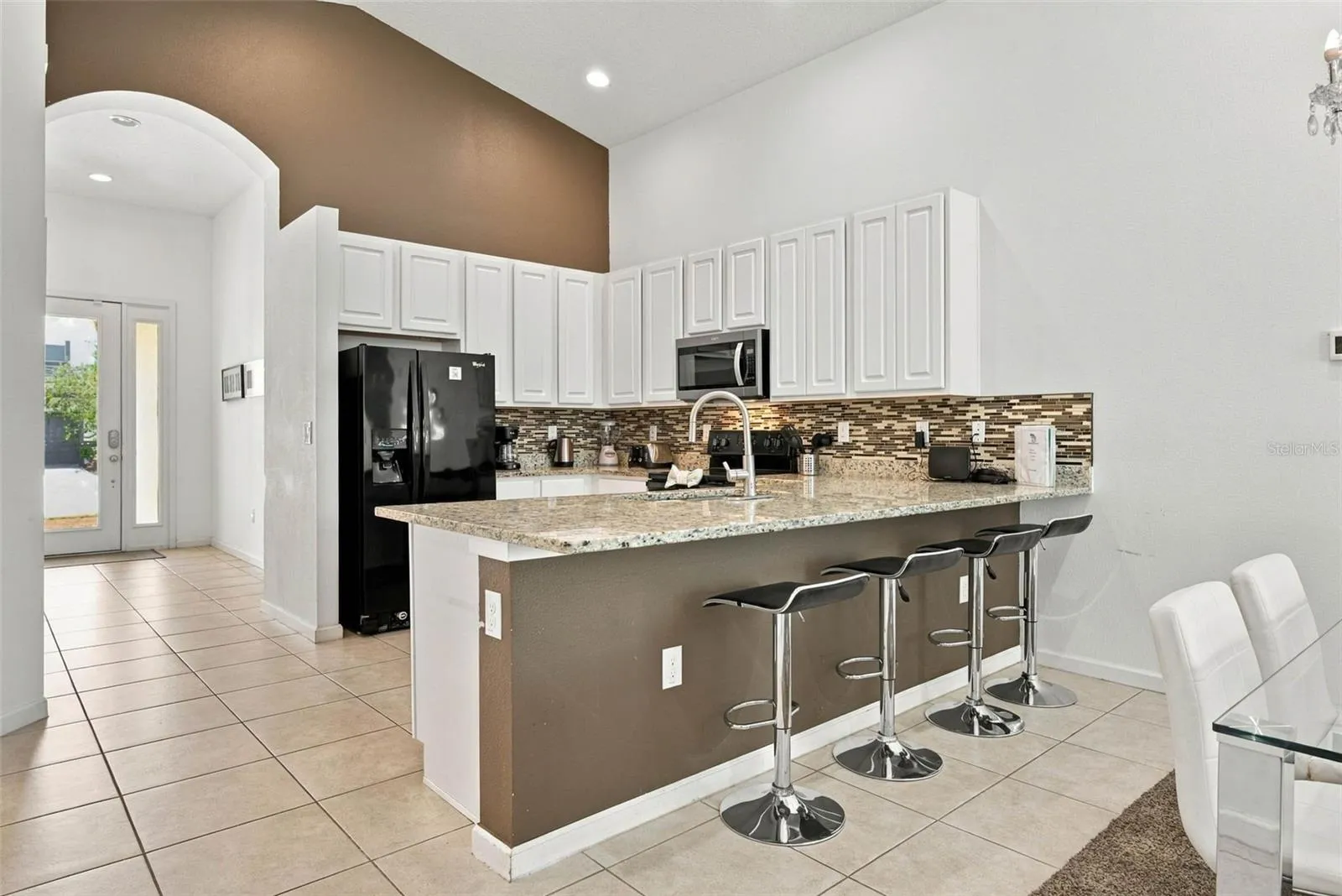 Open kitchen with 42" white cabinets, black Whirlpool appliances and granite countertops.
