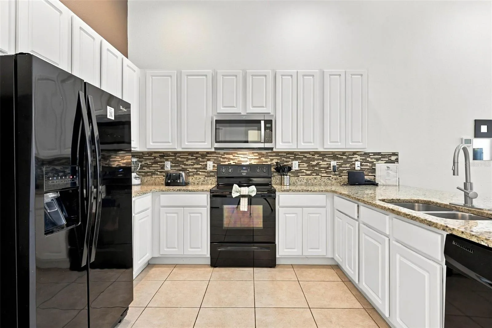 Open kitchen with 42" white cabinets, black Whirlpool appliances and granite countertops.