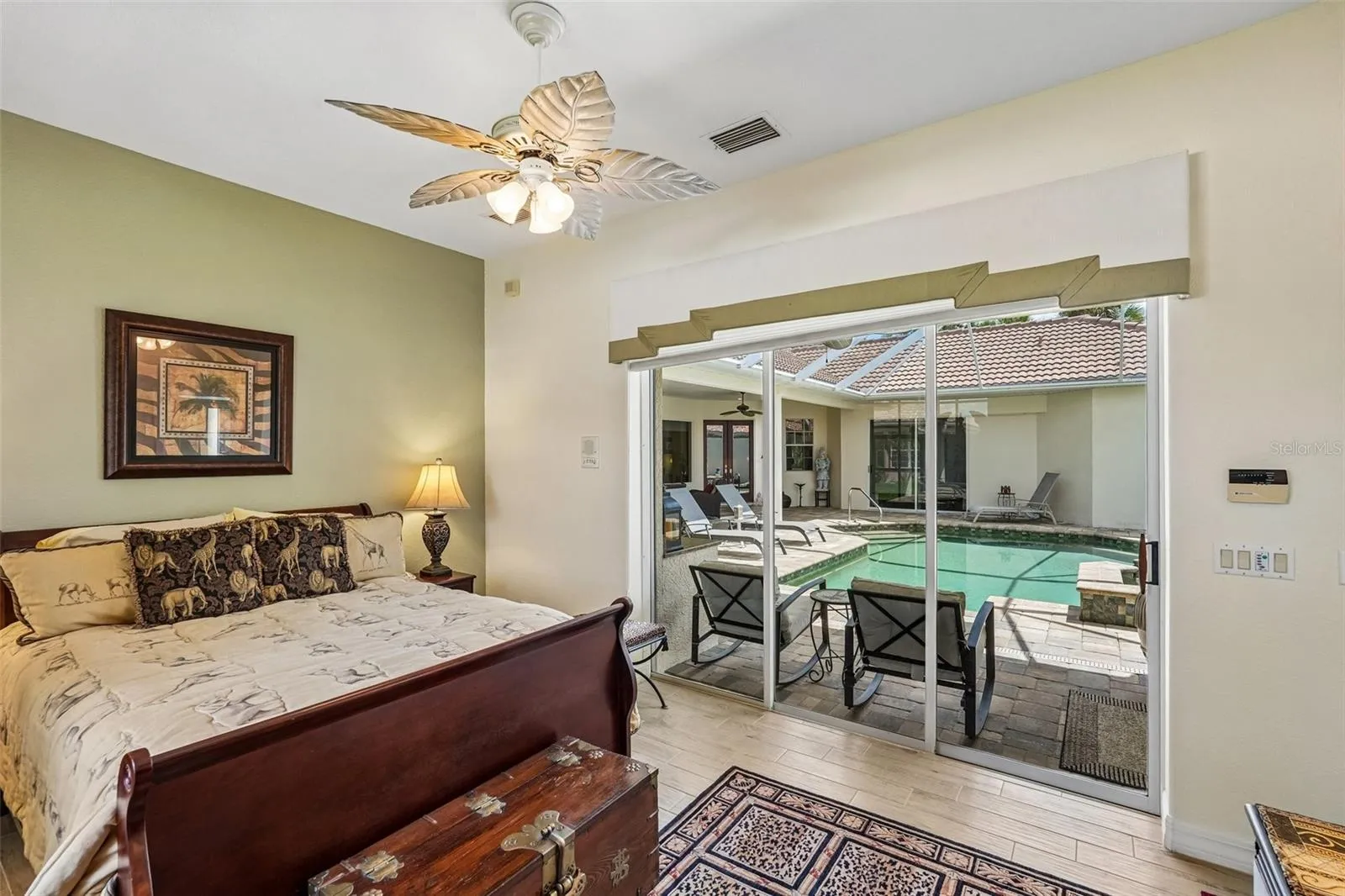 Bright guest suite featuring tile flooring, a palm-leaf ceiling fan, an en-suite bath and large sliding glass doors providing direct access and views to the screened pool deck