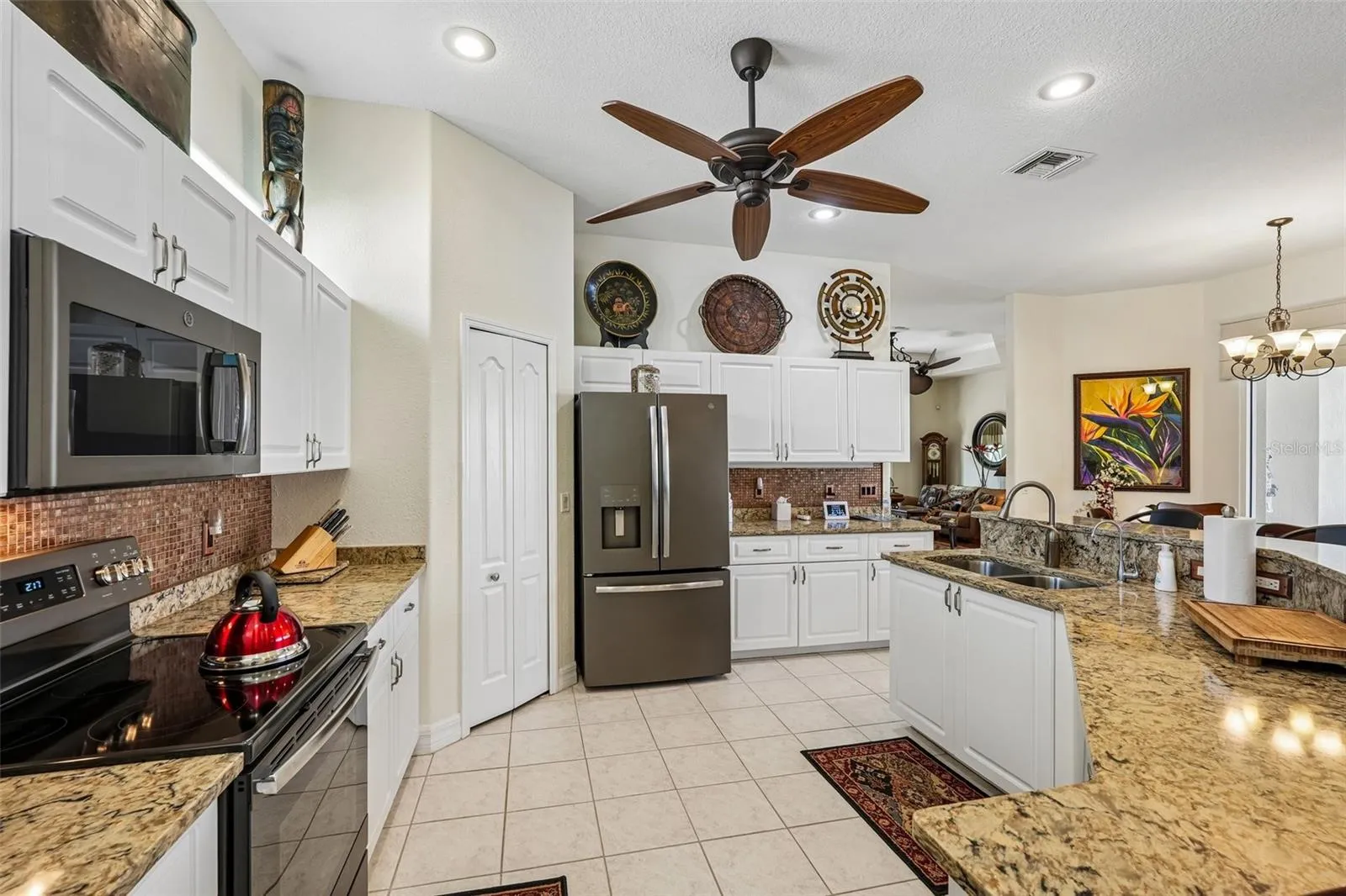 Bright, open-concept kitchen featuring rich granite countertops, crisp white cabinetry, a raised breakfast bar, and stainless steel/black appliances overlooking the main living and outdoor spaces