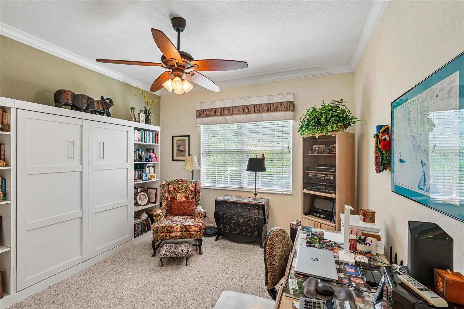 Versatile home office or guest bedroom featuring plush carpeting, Murphy Bed, crown molding, a wood-blade ceiling fan and a large window providing ample natural light
