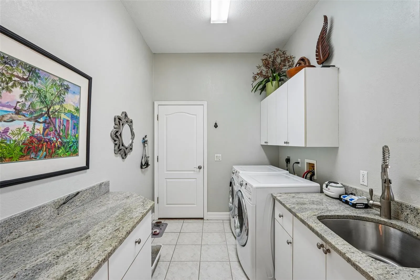 Laundry room featuring granite counter space, a built-in stainless steel utility sink, front-loading washer and dryer, tile flooring and upper and lower storage cabinets