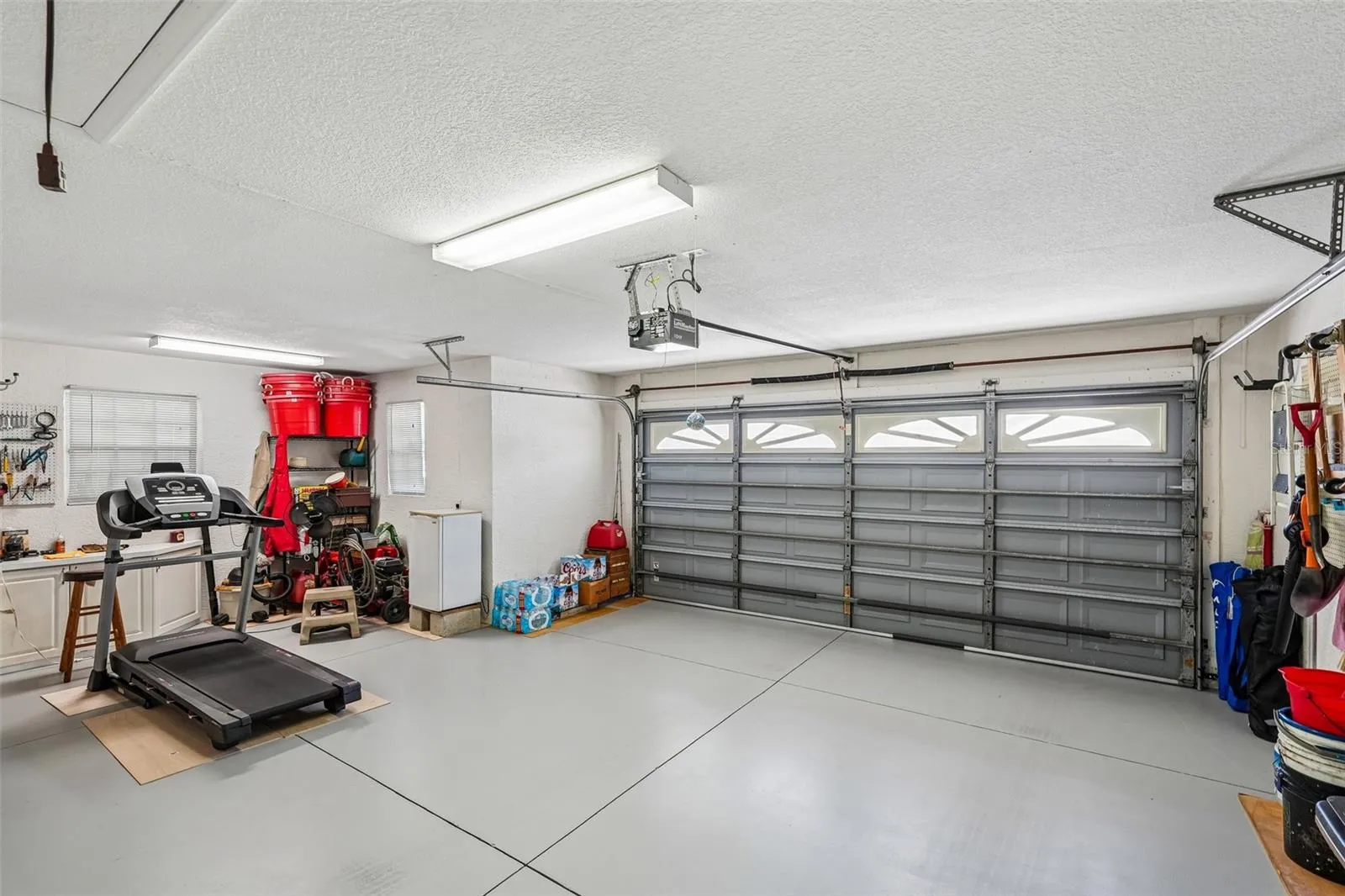 Spacious two and a half car garage featuring epoxy flooring, overhead fluorescent lighting, built-in wall cabinets, and an automatic garage door opener