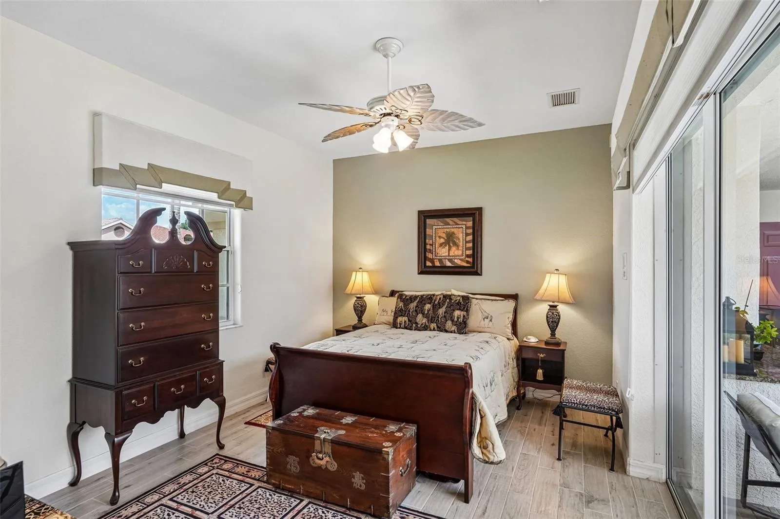 Bright guest suite featuring tile flooring, a palm-leaf ceiling fan, an en-suite bath and large sliding glass doors providing direct access and views to the screened pool deck