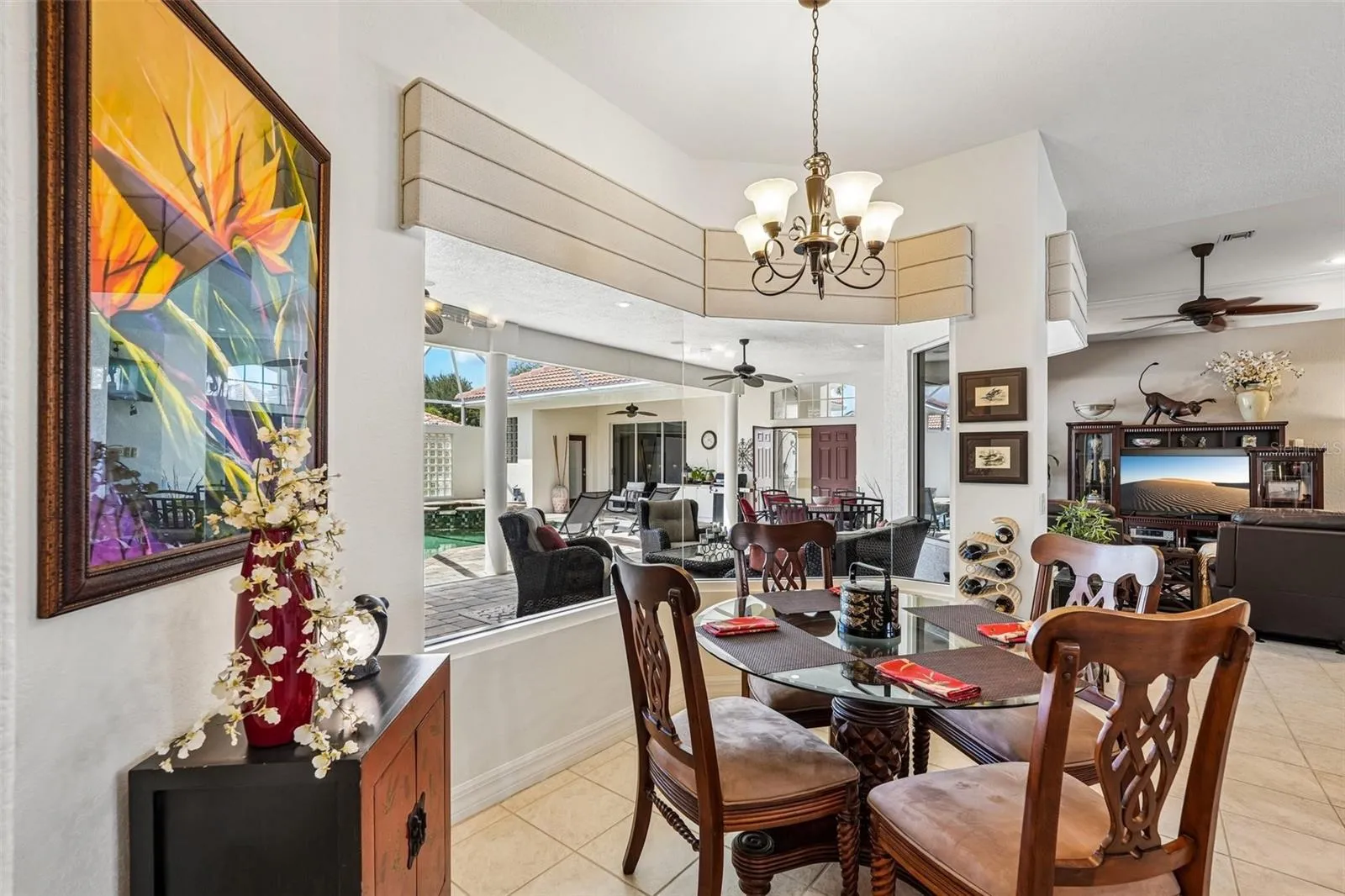 Sunlit breakfast nook featuring tile flooring, a decorative chandelier and floor-to-ceiling aquarium glass windows offering seamless, unobstructed views of the screened pool and lanai