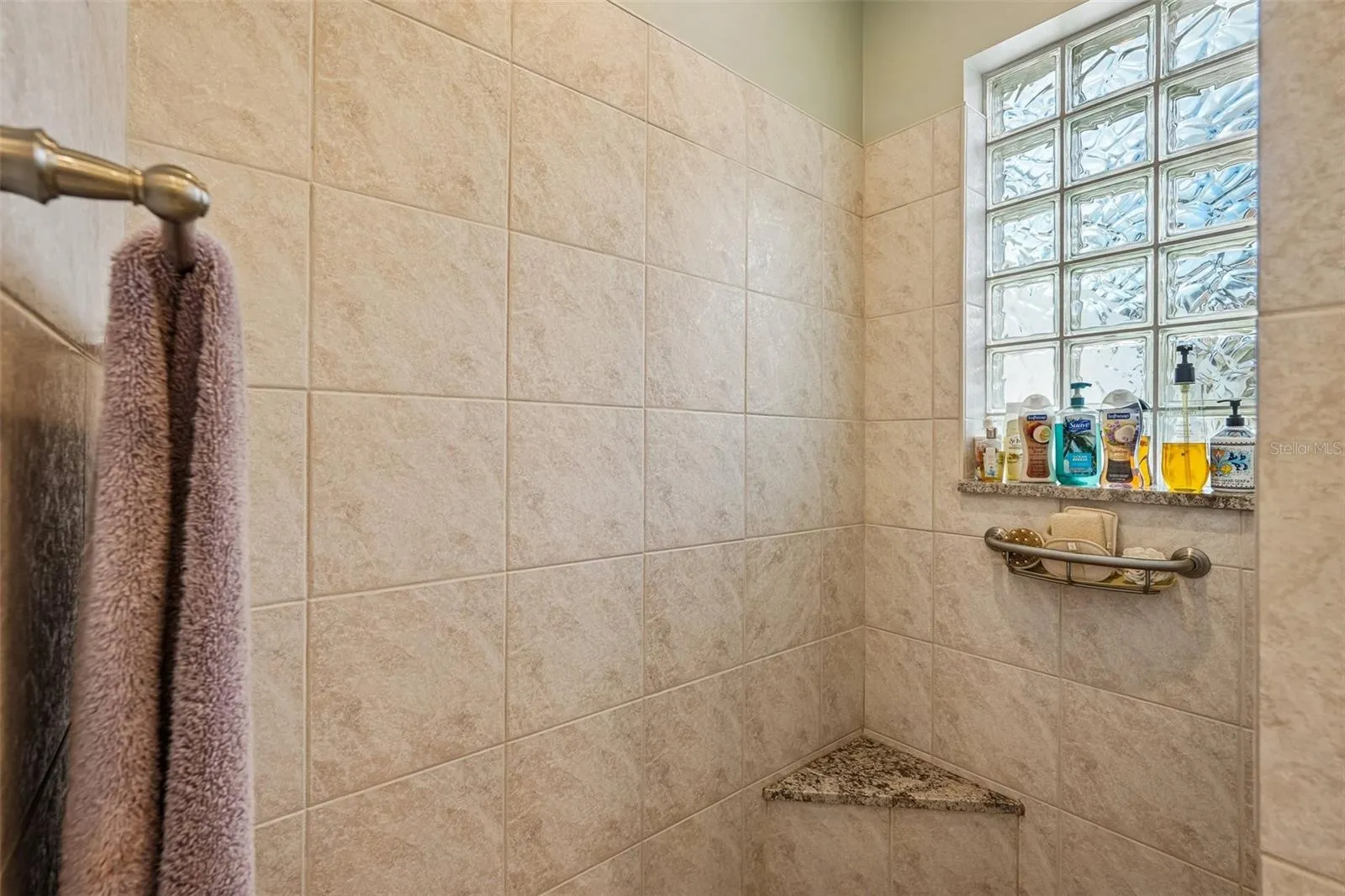 This luxurious primary en-suite bathroom boasts a expansive dual-sink vanity with granite countertops, ample storage cabinetry, a deep soaking tub and a separate tiled walk-in shower with glass block accents for privacy and light