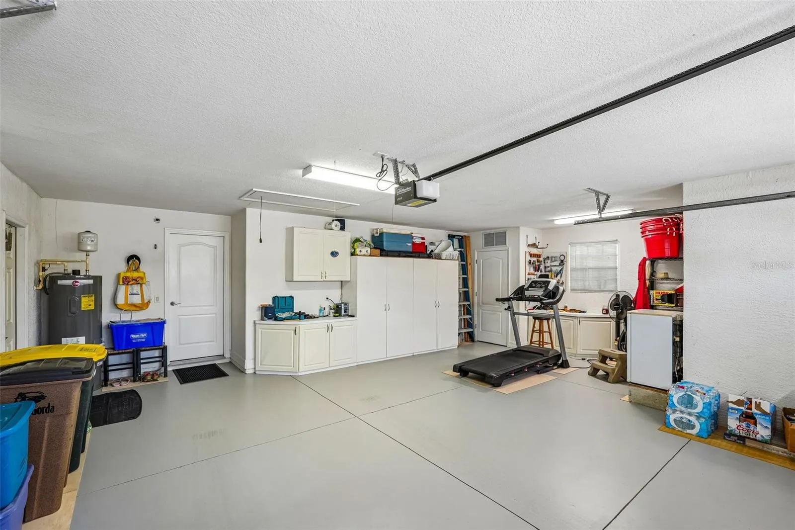 Spacious two and a half car garage featuring epoxy flooring, overhead fluorescent lighting, built-in wall cabinets, and an automatic garage door opener