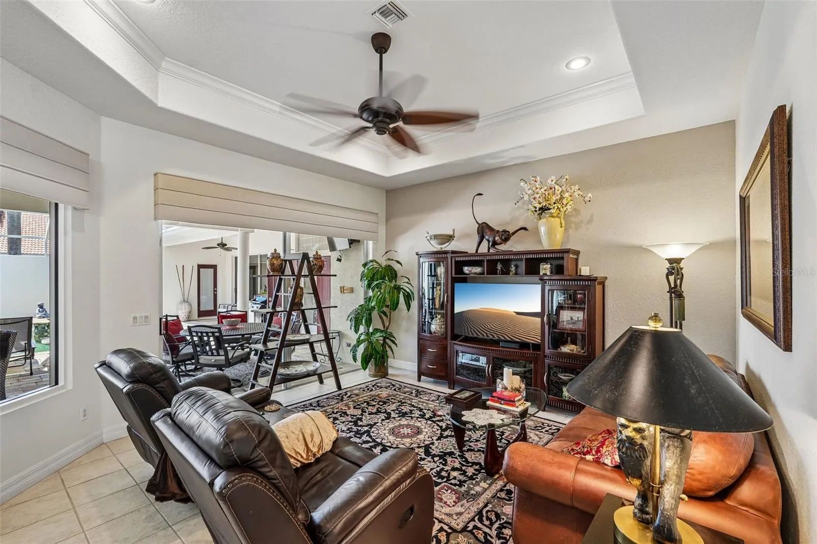 Inviting living area featuring warm wood floors, tray ceilings with crown molding, a dual-head tropical fan, and french doors offering seamless access to lush outdoor views