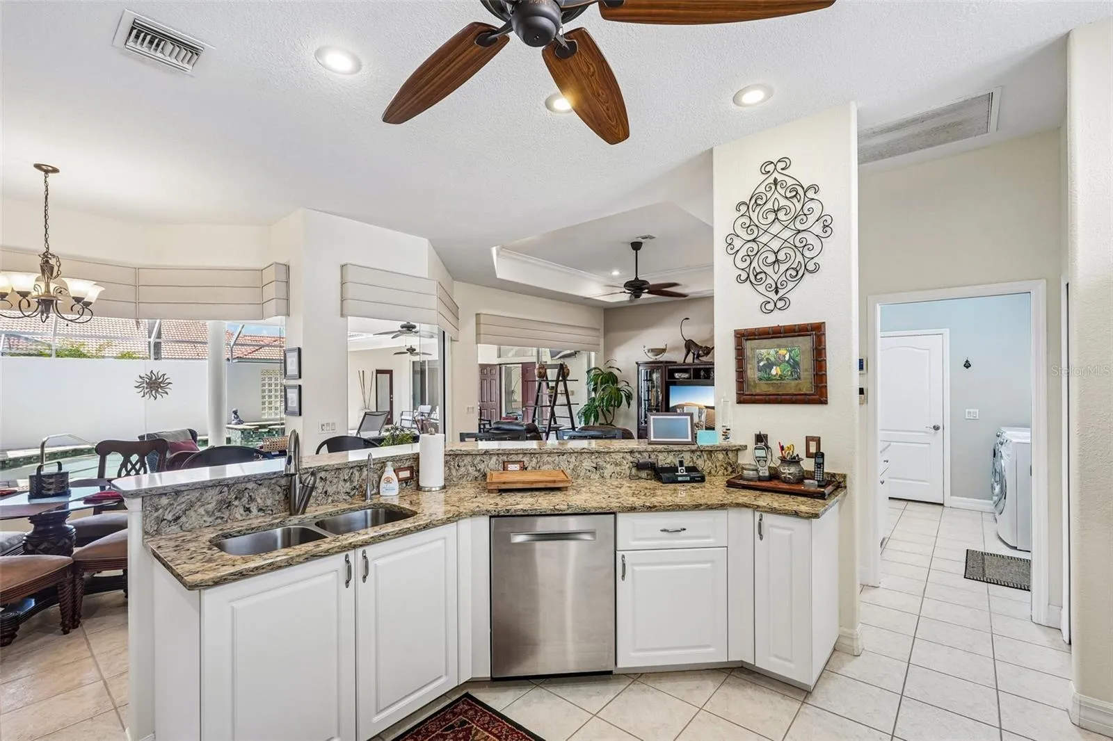 Bright, open-concept kitchen featuring rich granite countertops, crisp white cabinetry, a raised breakfast bar, and stainless steel/black appliances overlooking the main living and outdoor spaces
