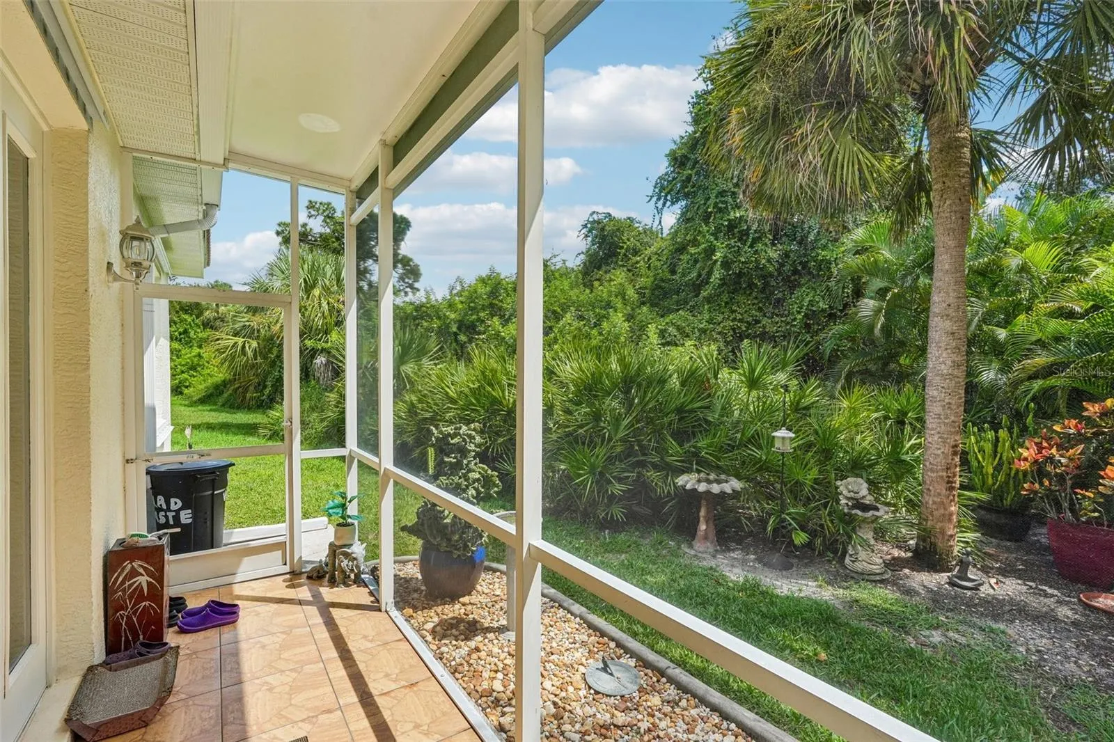 Private screened porch featuring tiled flooring, a screen door for yard access and peaceful views of the surrounding tropical landscaping