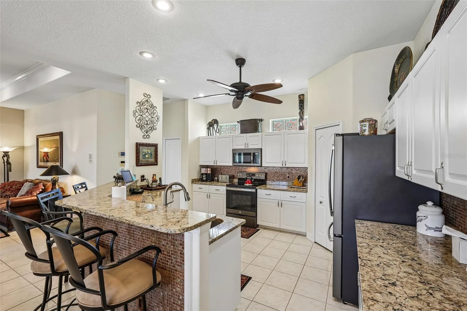 Bright, open-concept kitchen featuring rich granite countertops, crisp white cabinetry, a raised breakfast bar, and stainless steel/black appliances overlooking the main living and outdoor spaces