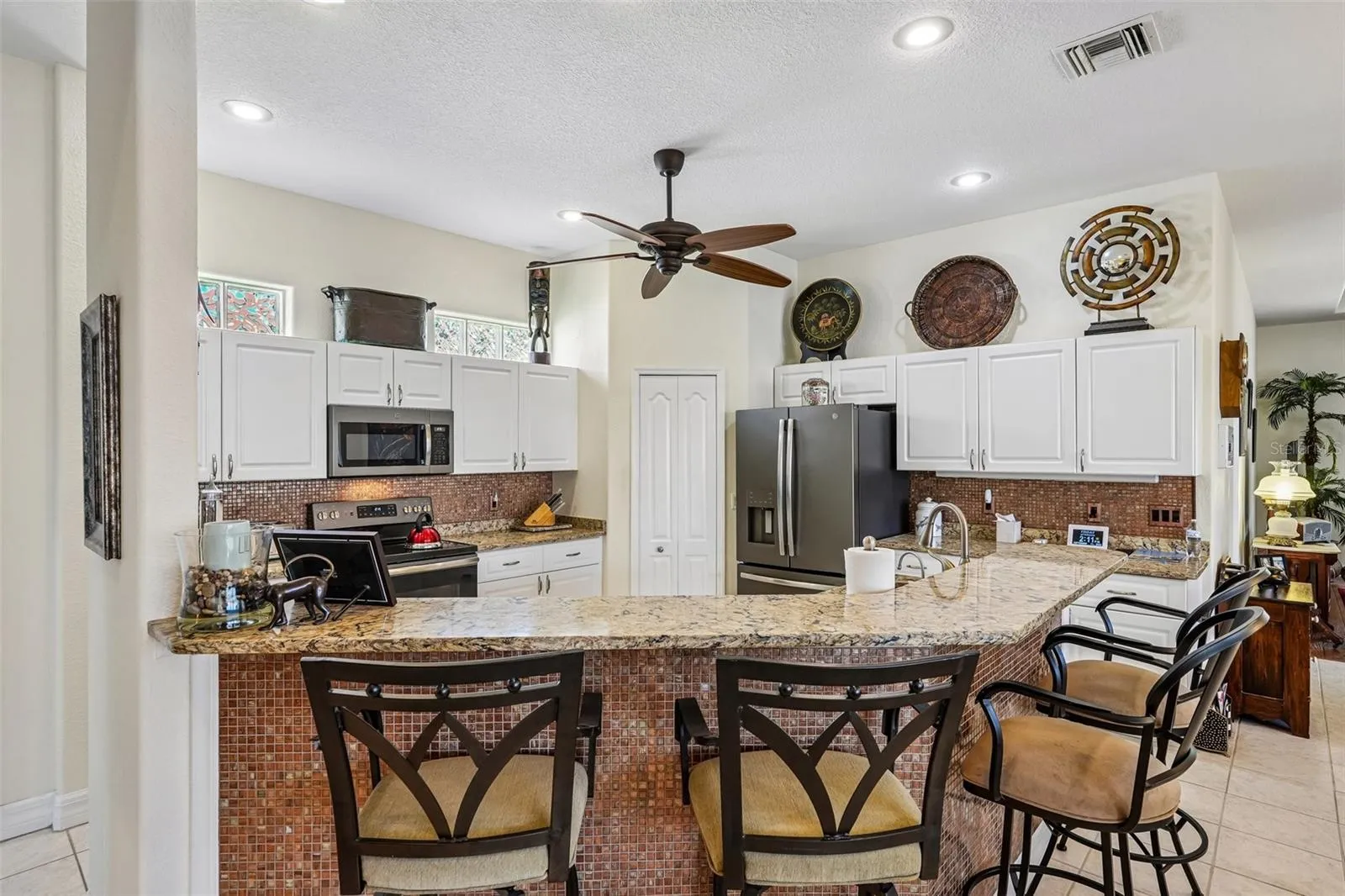 Bright, open-concept kitchen featuring rich granite countertops, crisp white cabinetry, a raised breakfast bar, and stainless steel/black appliances overlooking the main living and outdoor spaces