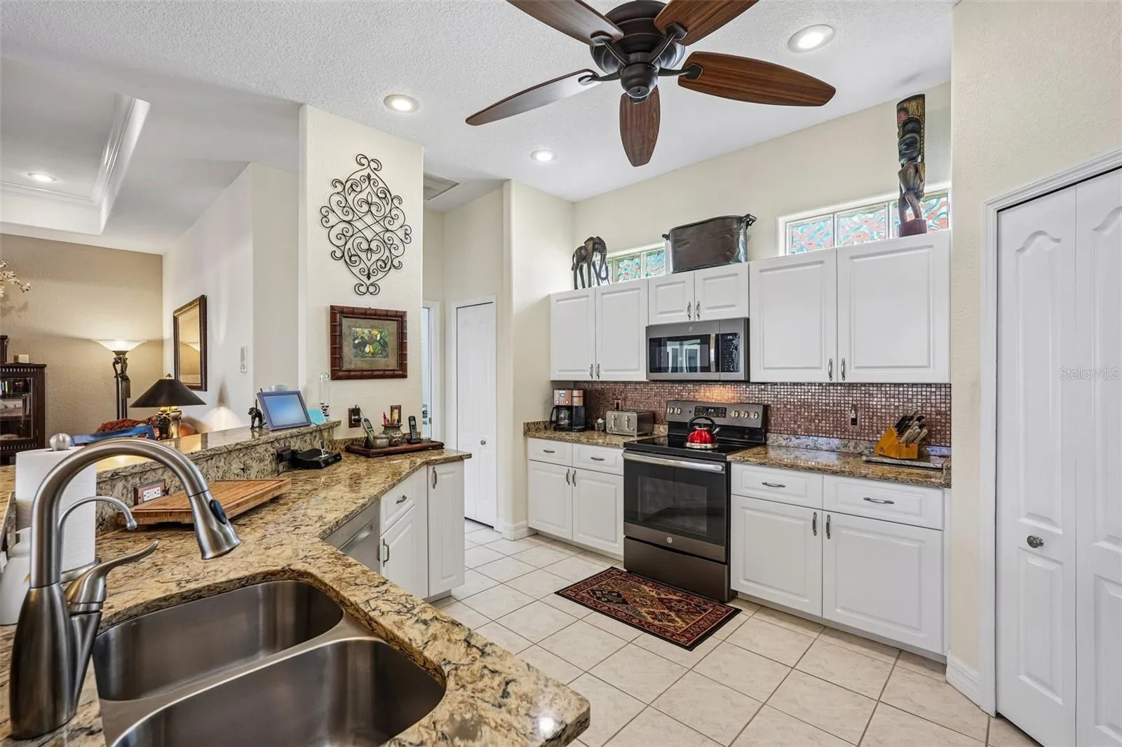 Bright, open-concept kitchen featuring rich granite countertops, crisp white cabinetry, a raised breakfast bar, and stainless steel/black appliances overlooking the main living and outdoor spaces