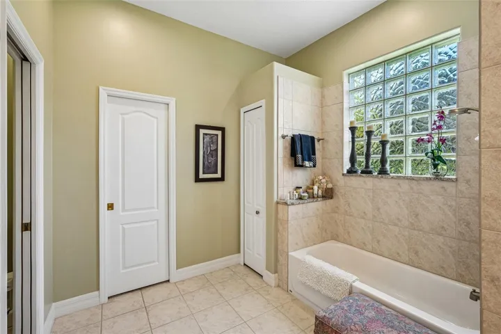 This luxurious primary en-suite bathroom boasts a expansive dual-sink vanity with granite countertops, ample storage cabinetry, a deep soaking tub and a separate tiled walk-in shower with glass block accents for privacy and light