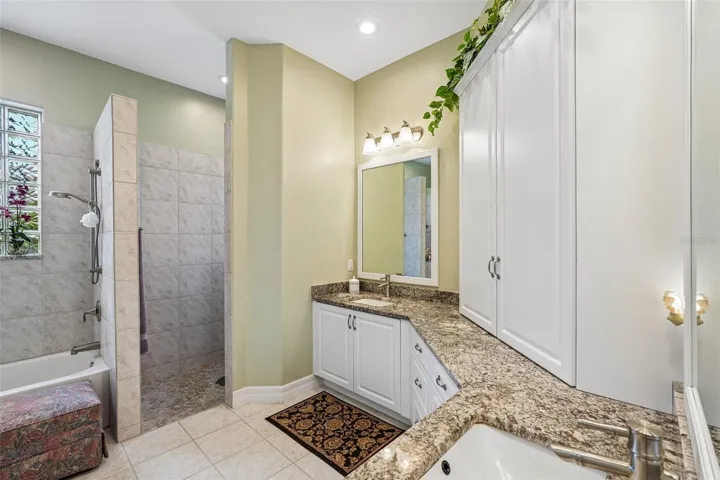 This luxurious primary en-suite bathroom boasts a expansive dual-sink vanity with granite countertops, ample storage cabinetry, a deep soaking tub and a separate tiled walk-in shower with glass block accents for privacy and light