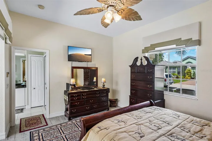 Bright guest suite featuring tile flooring, a palm-leaf ceiling fan, an en-suite bath and large sliding glass doors providing direct access and views to the screened pool deck