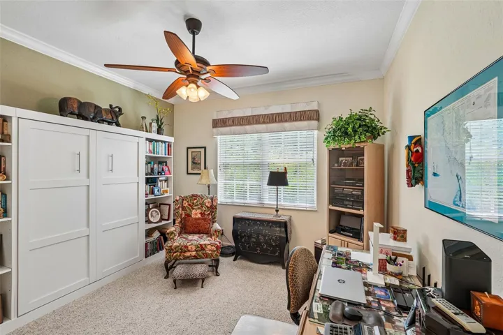 Versatile home office or guest bedroom featuring plush carpeting, Murphy Bed, crown molding, a wood-blade ceiling fan and a large window providing ample natural light