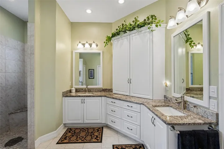 This luxurious primary en-suite bathroom boasts a expansive dual-sink vanity with granite countertops, ample storage cabinetry, a deep soaking tub and a separate tiled walk-in shower with glass block accents for privacy and light
