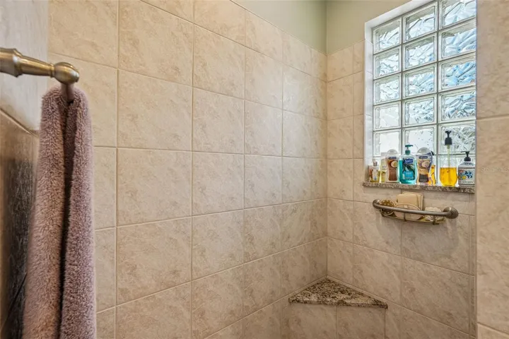 This luxurious primary en-suite bathroom boasts a expansive dual-sink vanity with granite countertops, ample storage cabinetry, a deep soaking tub and a separate tiled walk-in shower with glass block accents for privacy and light