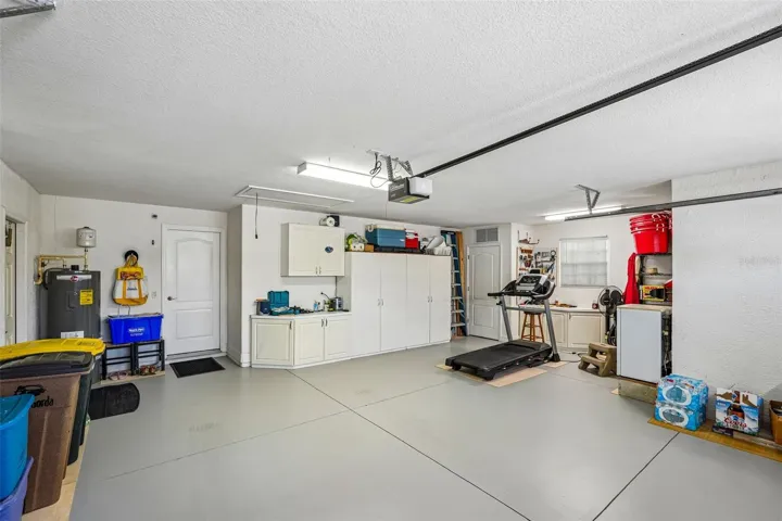 Spacious two and a half car garage featuring epoxy flooring, overhead fluorescent lighting, built-in wall cabinets, and an automatic garage door opener