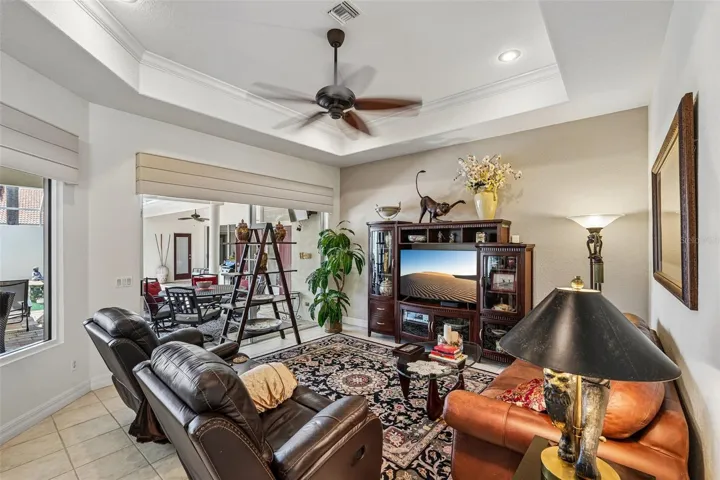 Inviting living area featuring warm wood floors, tray ceilings with crown molding, a dual-head tropical fan, and french doors offering seamless access to lush outdoor views