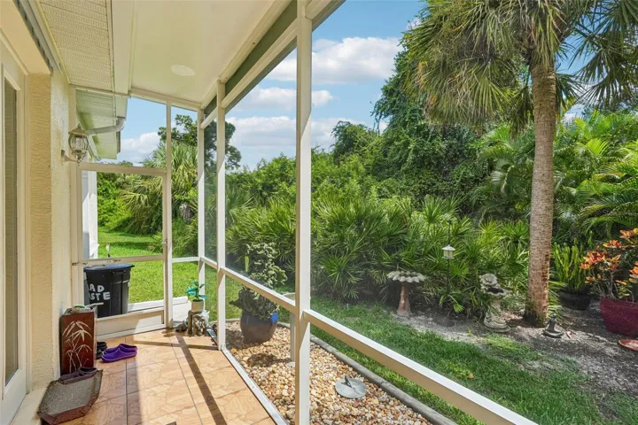 Private screened porch featuring tiled flooring, a screen door for yard access and peaceful views of the surrounding tropical landscaping