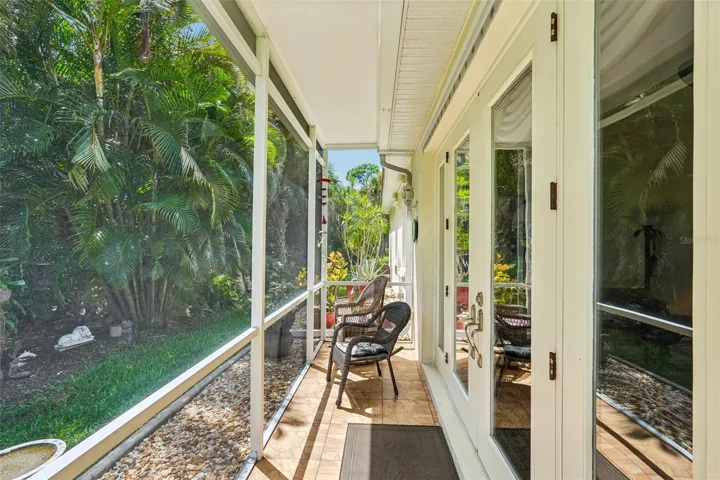 Private screened porch featuring tiled flooring, a screen door for yard access and peaceful views of the surrounding tropical landscaping
