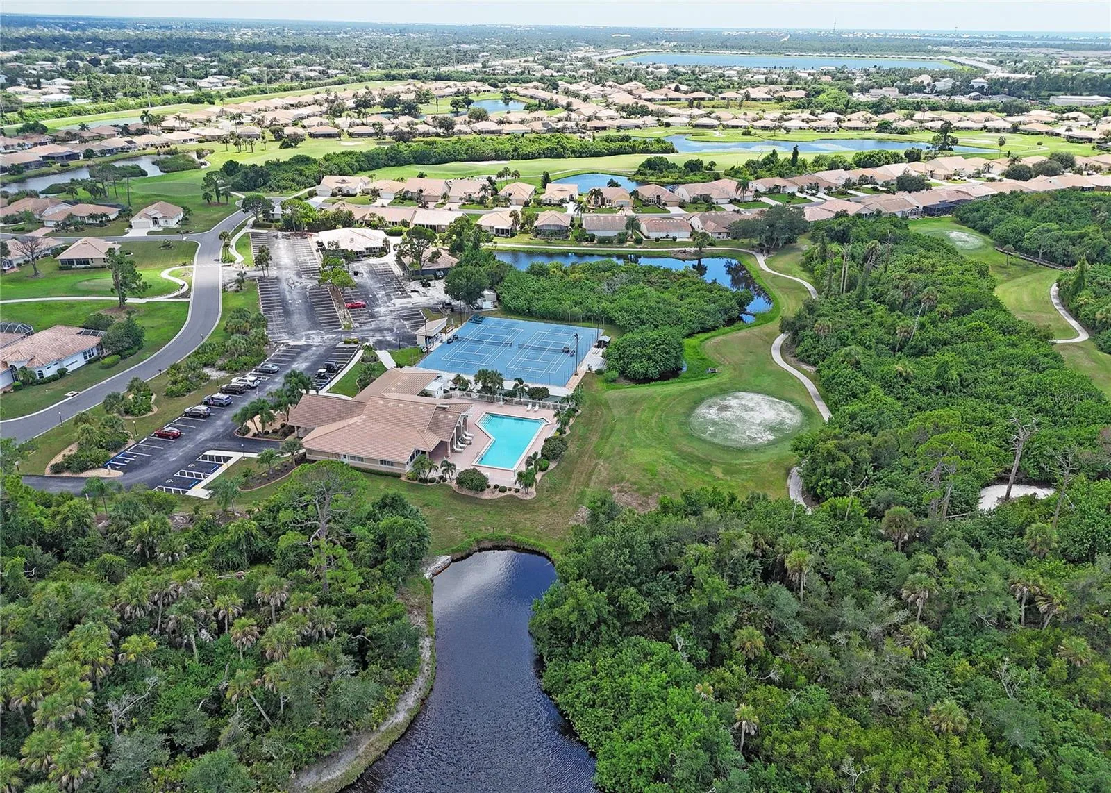 Clubhouse with pool and tennis courts nestled within greenery and water.
