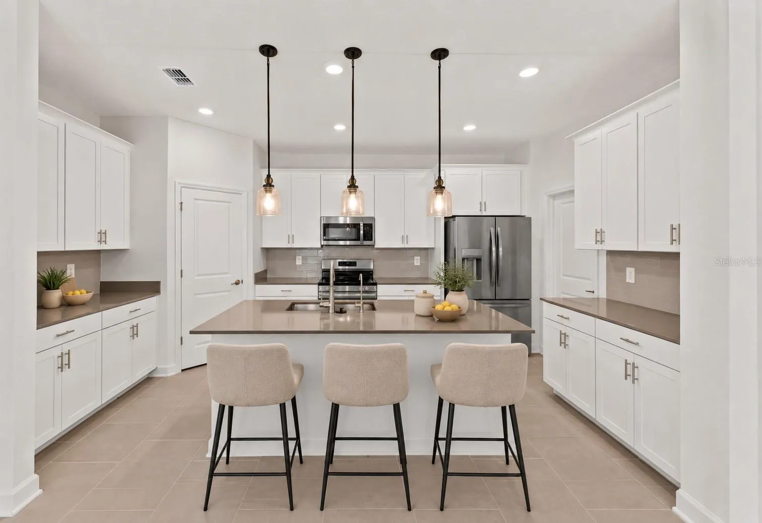 At the heart of the home, the kitchen features shaker style cabinetry, quartz countertops, stainless steel appliances, a tiled backsplash, pantry storage and a large island with breakfast bar seating beneath pendant lighting.
