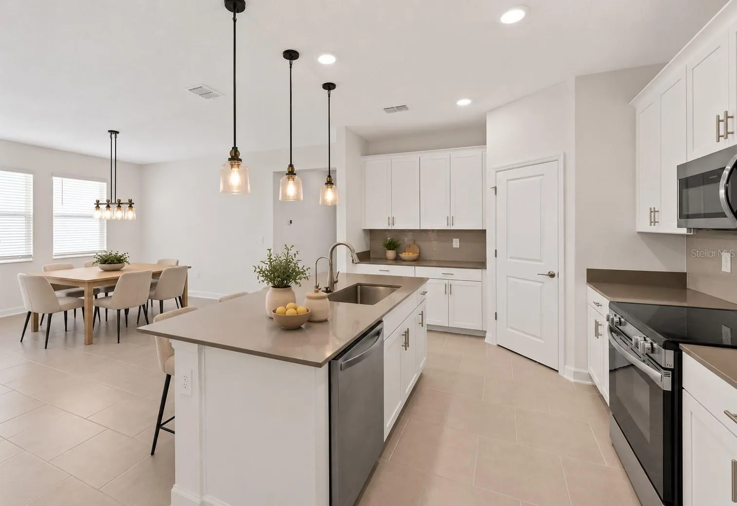 At the heart of the home, the kitchen features shaker style cabinetry, quartz countertops, stainless steel appliances, a tiled backsplash, pantry storage and a large island with breakfast bar seating beneath pendant lighting.