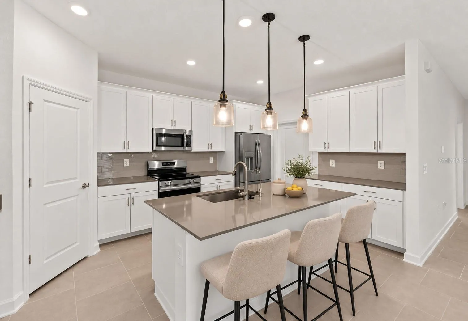 At the heart of the home, the kitchen features shaker style cabinetry, quartz countertops, stainless steel appliances, a tiled backsplash, pantry storage and a large island with breakfast bar seating beneath pendant lighting.