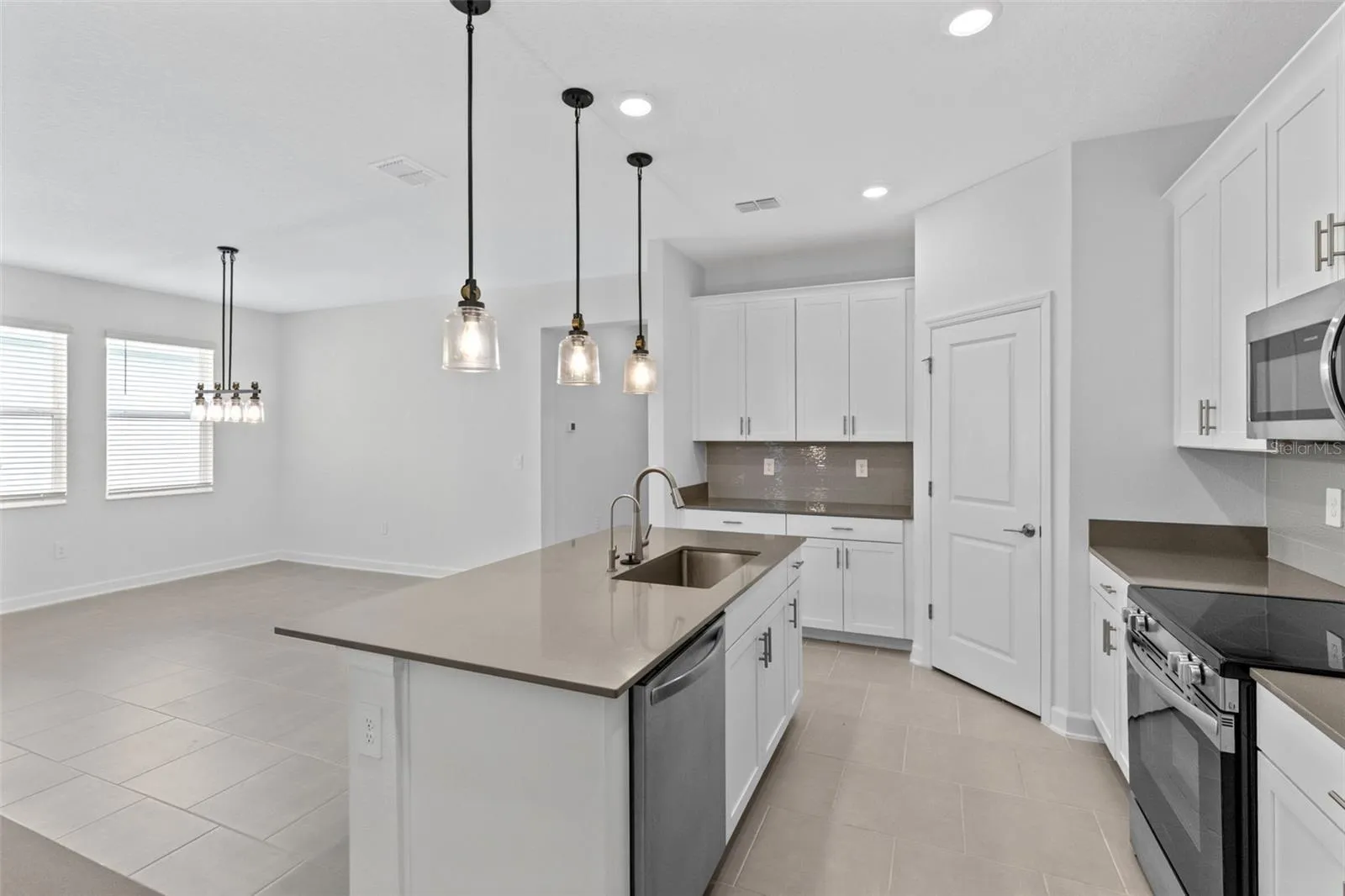At the heart of the home, the kitchen features shaker style cabinetry, quartz countertops, stainless steel appliances, a tiled backsplash, pantry storage and a large island with breakfast bar seating beneath pendant lighting.