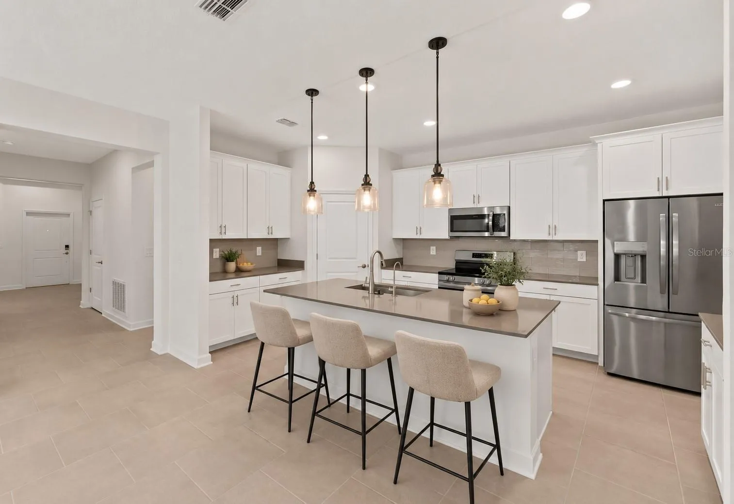 At the heart of the home, the kitchen features shaker style cabinetry, quartz countertops, stainless steel appliances, a tiled backsplash, pantry storage and a large island with breakfast bar seating beneath pendant lighting.