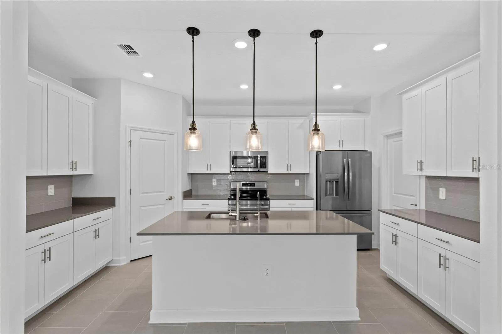 At the heart of the home, the kitchen features shaker style cabinetry, quartz countertops, stainless steel appliances, a tiled backsplash, pantry storage and a large island with breakfast bar seating beneath pendant lighting.