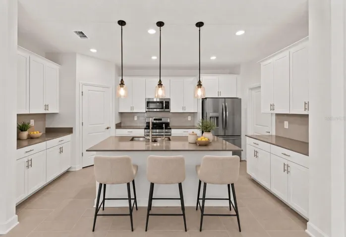 At the heart of the home, the kitchen features shaker style cabinetry, quartz countertops, stainless steel appliances, a tiled backsplash, pantry storage and a large island with breakfast bar seating beneath pendant lighting.