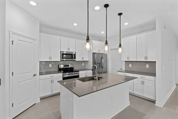 At the heart of the home, the kitchen features shaker style cabinetry, quartz countertops, stainless steel appliances, a tiled backsplash, pantry storage and a large island with breakfast bar seating beneath pendant lighting.