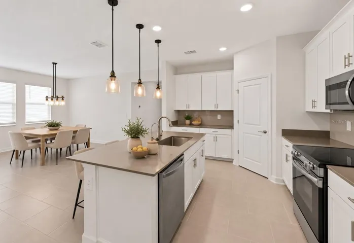 At the heart of the home, the kitchen features shaker style cabinetry, quartz countertops, stainless steel appliances, a tiled backsplash, pantry storage and a large island with breakfast bar seating beneath pendant lighting.
