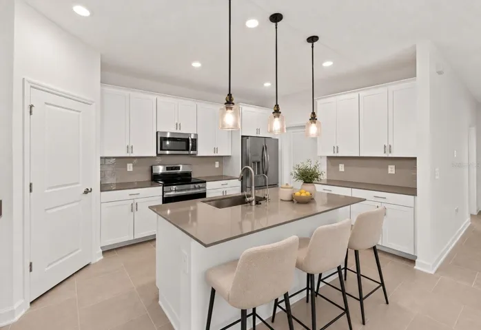 At the heart of the home, the kitchen features shaker style cabinetry, quartz countertops, stainless steel appliances, a tiled backsplash, pantry storage and a large island with breakfast bar seating beneath pendant lighting.